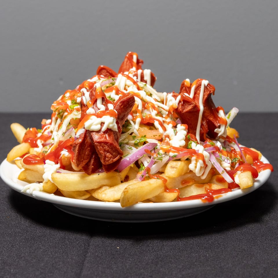 Pika's Restaurant's Ecuadorian salchipapa, a mound of fries topped with sliced hot dogs, sauces, and vegetables.