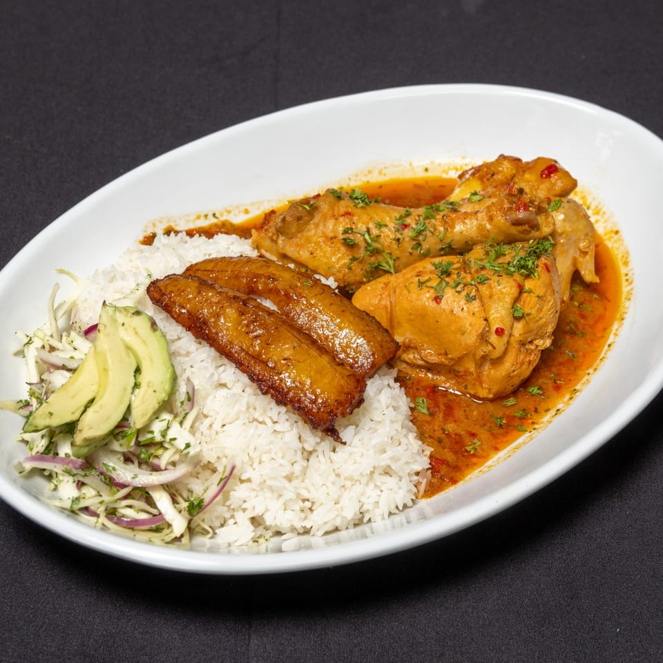 Ecuadorian chicken stew with rice, fried plantains, and avocado salad on a white plate.