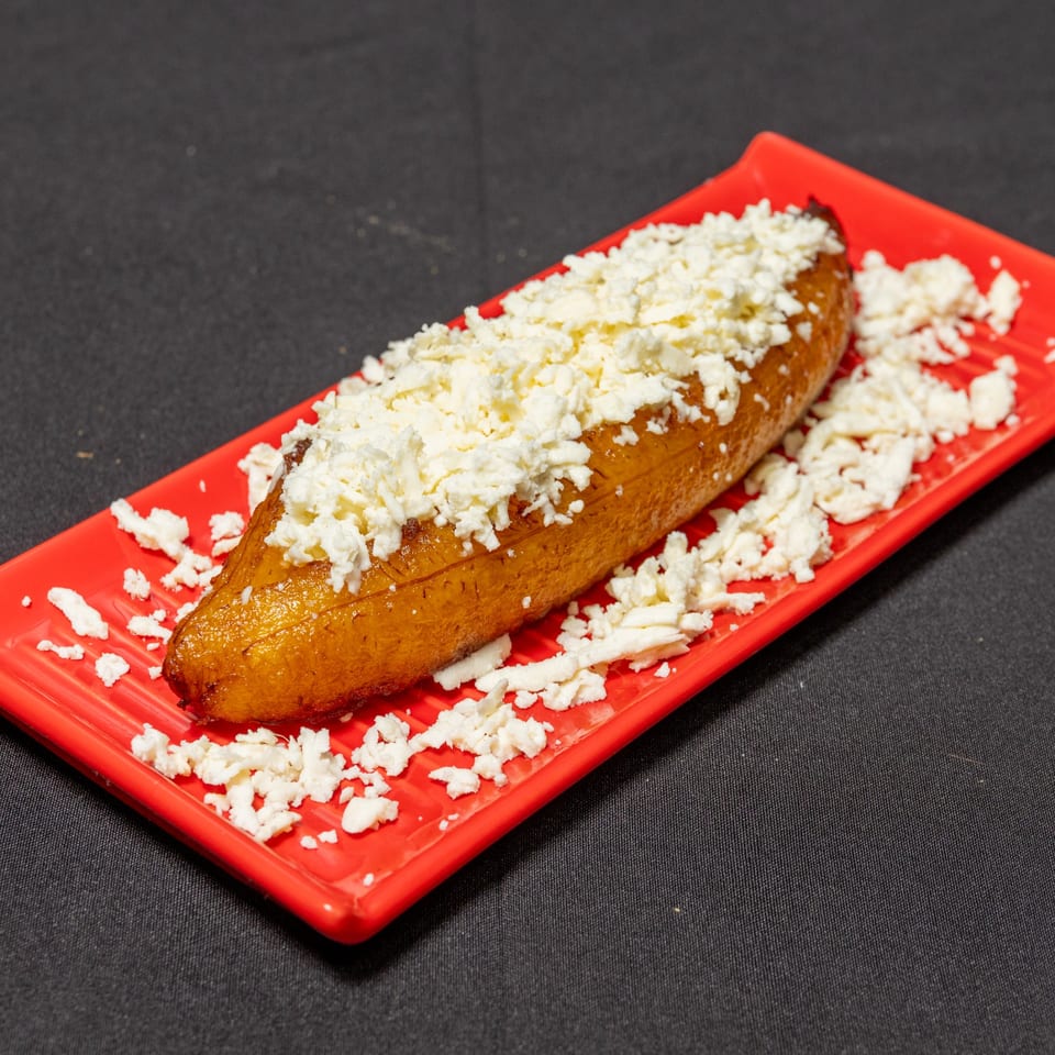 Sweet plantain topped with crumbled white cheese, served on a red rectangular plate.