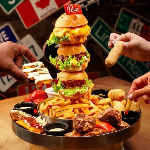 A Pika's Restaurant platter with a tower of three burgers, fries, meat, and other appetizers.