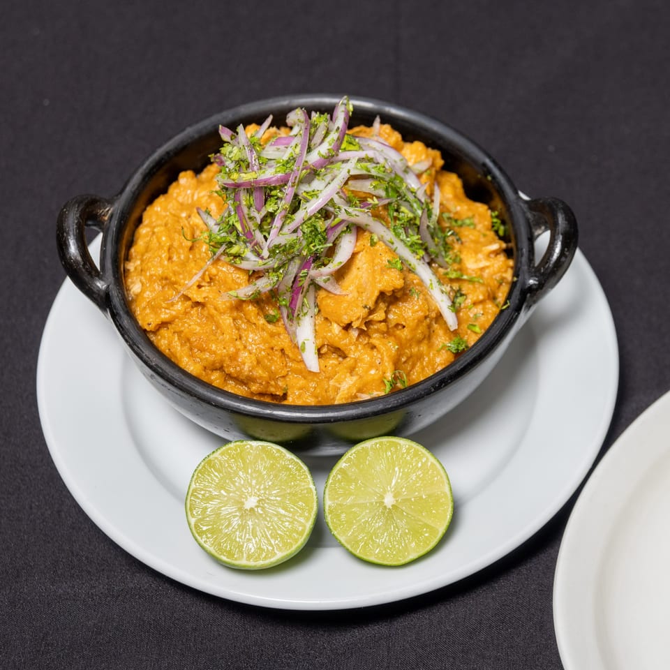 Ecuadorian dish in a black bowl, topped with red onions and cilantro, served with lime halves.