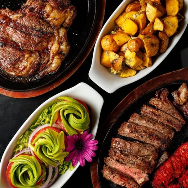 Grilled steak, sliced steak, roasted potatoes, and a salad with avocado roses, tomatoes, and onions.
