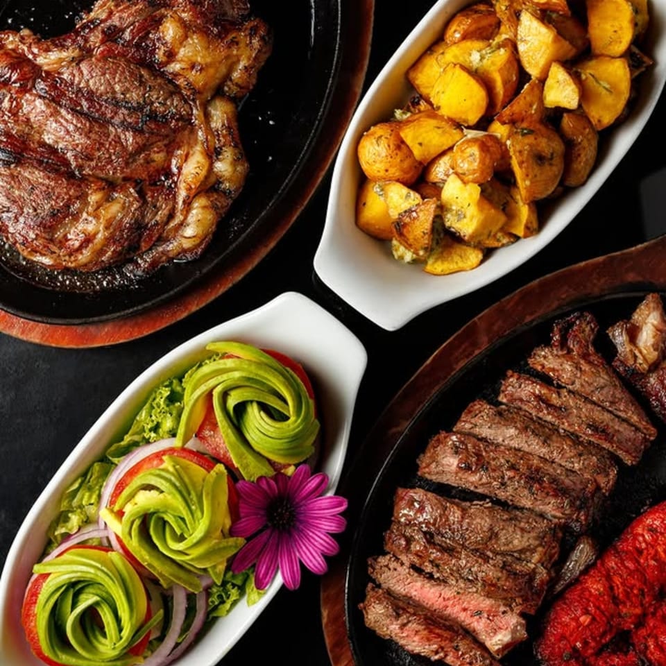 Grilled steak, sliced steak, roasted potatoes, and a salad with avocado roses, tomatoes, and onions.