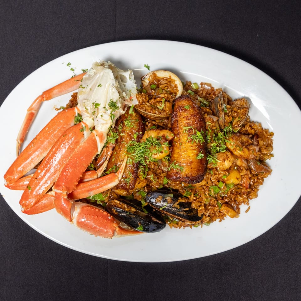 Ecuadorian seafood rice with crab legs, mussels, clams, shrimp, and plantains on a white plate.