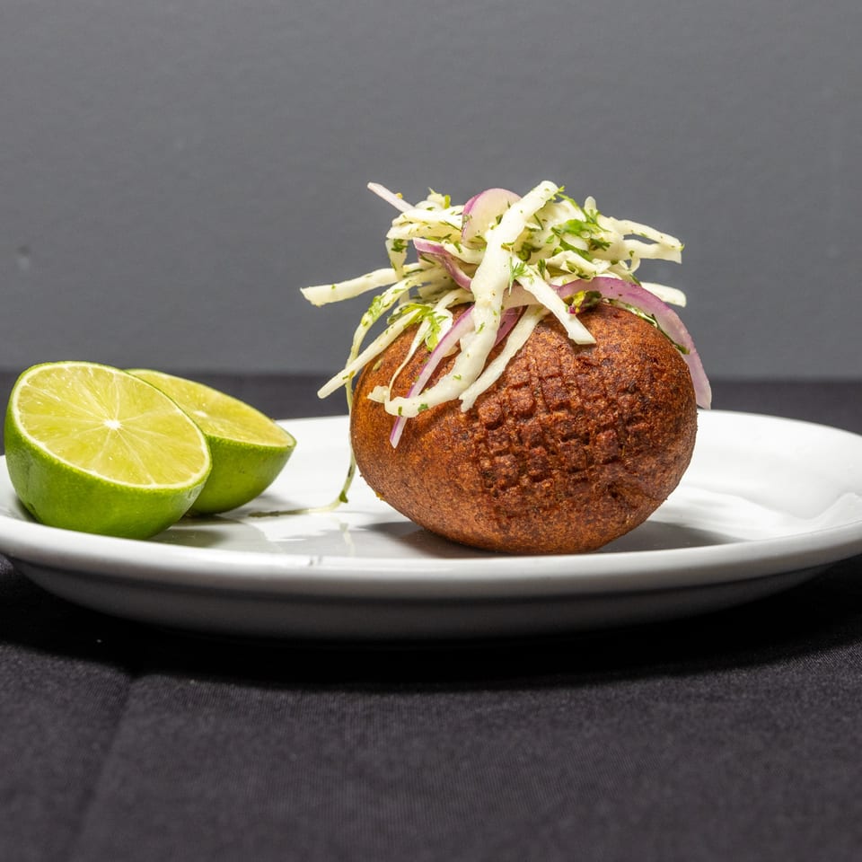 A Pika's Restaurant llapingacho, a fried potato patty, topped with cabbage and red onion, with lime halves.