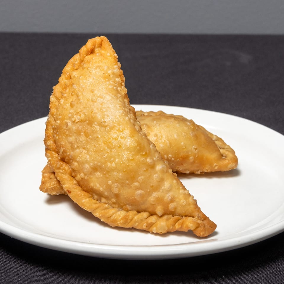 Two golden-brown, crispy empanadas with crimped edges on a white plate.
