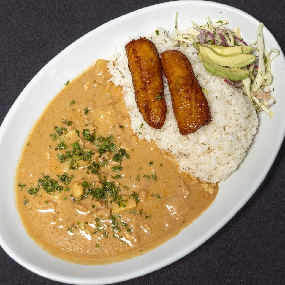 Ecuadorian dish with creamy stew, white rice, fried plantains, and a side salad with avocado.