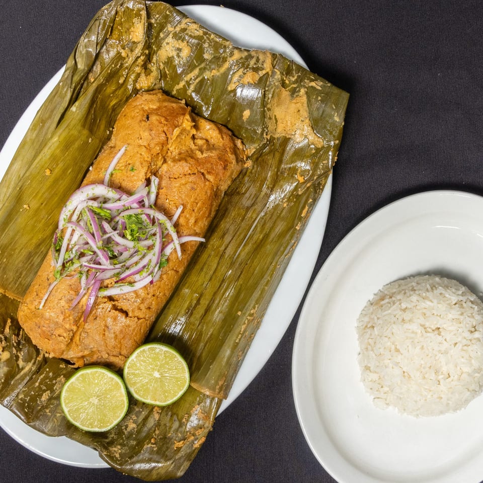 Ecuadorian humita, a corn tamale wrapped in a banana leaf, with red onions, cilantro, and lime, served with rice.